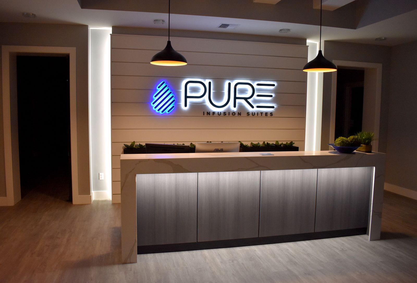 Reception desk under the illuminated PURE Infusion Suites sign at dusk