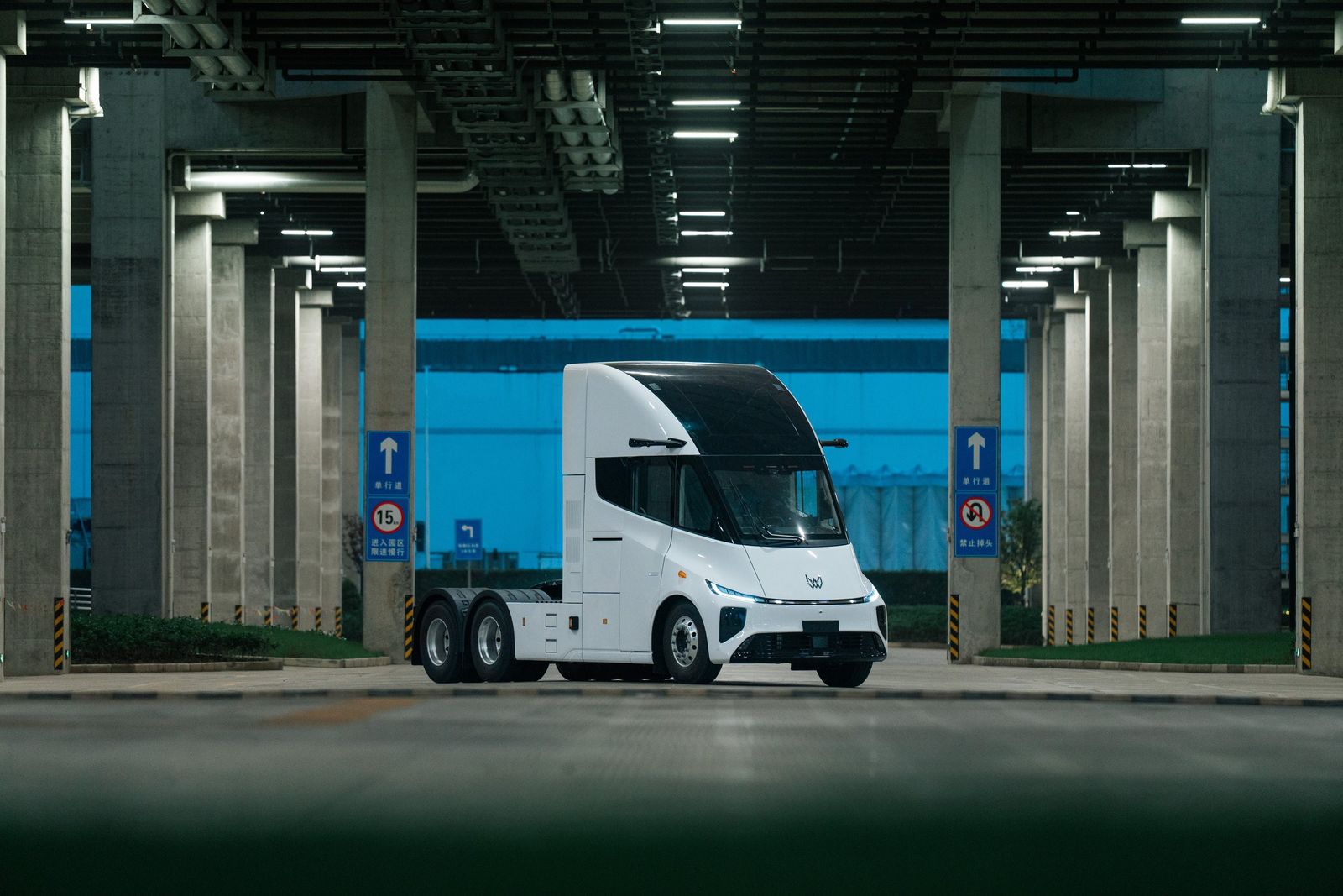 A white Xos electric semi tractor under a concrete overpass